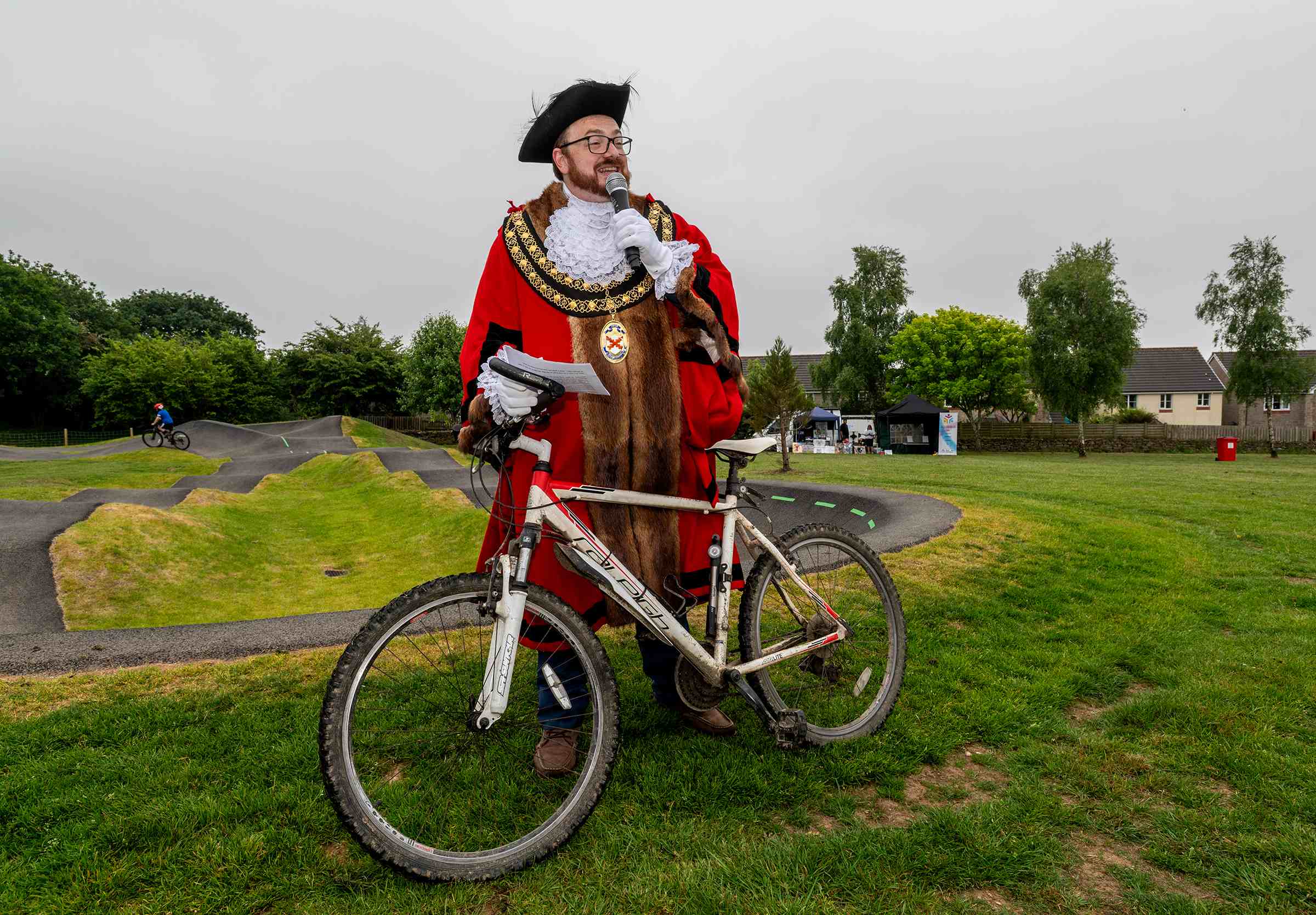 Cllr Ethan Stephens makes a speech next to the pump track, posing with a bike